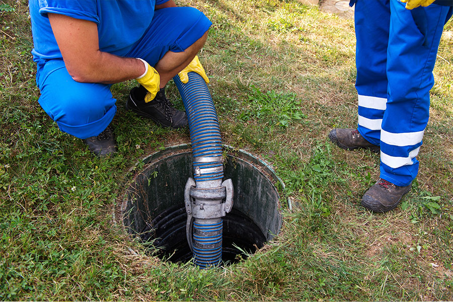 Two plumbers standing by a septic tank and a large blue pump to remove excess water from filling a septic tank in Springfield, IL