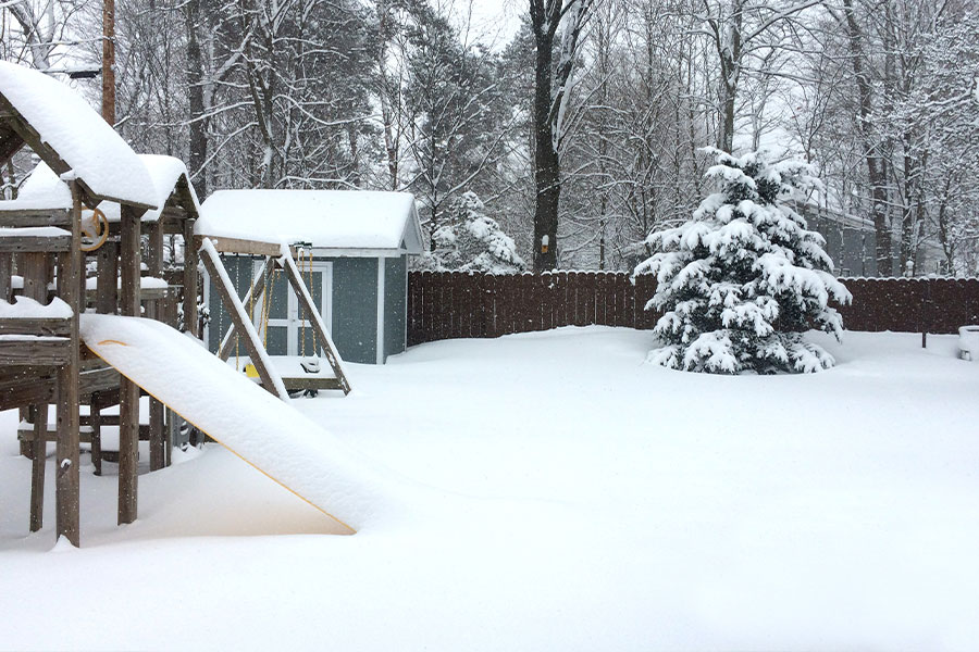 A residential backyard in Springfield, IL with a playground set, shed, and yard with a septic tank manhole covered in snow.