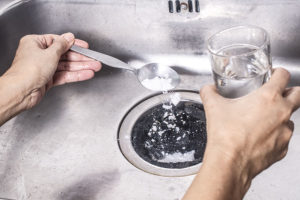 A homeowner using a homemade mixture of baking soda and vinegar to clean the inside of garbage disposal and plumbing stem in Decatur, IL.