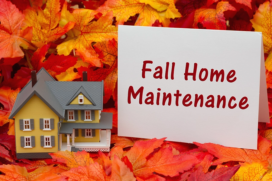 A small model house surrounded by fall leaves next to a sign that says “Fall Home Maintenance” in Decatur, IL.