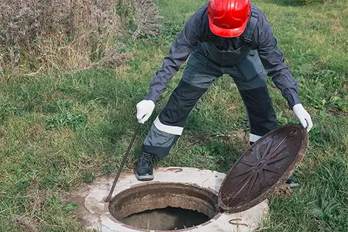 Sewer & Septic Specialists— A septic specialist in a blue uniform & red safety hat inspecting a septic tank in Decatur, IL.