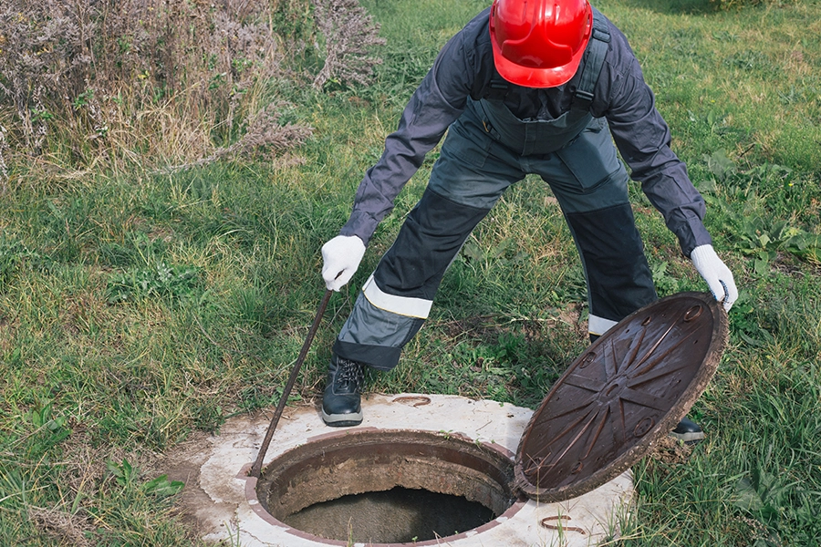 Sewer & Septic Specialists— A septic specialist in a blue uniform & red safety hat inspecting a septic tank in Decatur, IL.