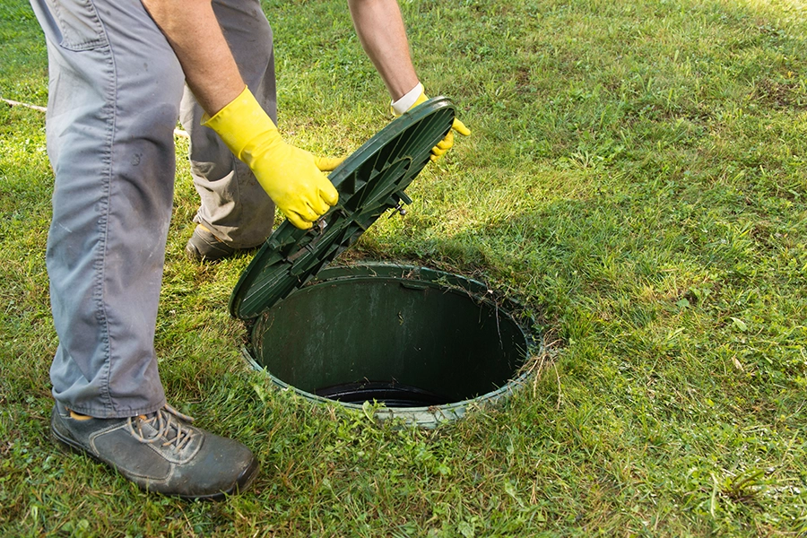 Sewer & Septic Specialists—A male plumber lifting a septic tank lid on a private property in Decatur, IL.