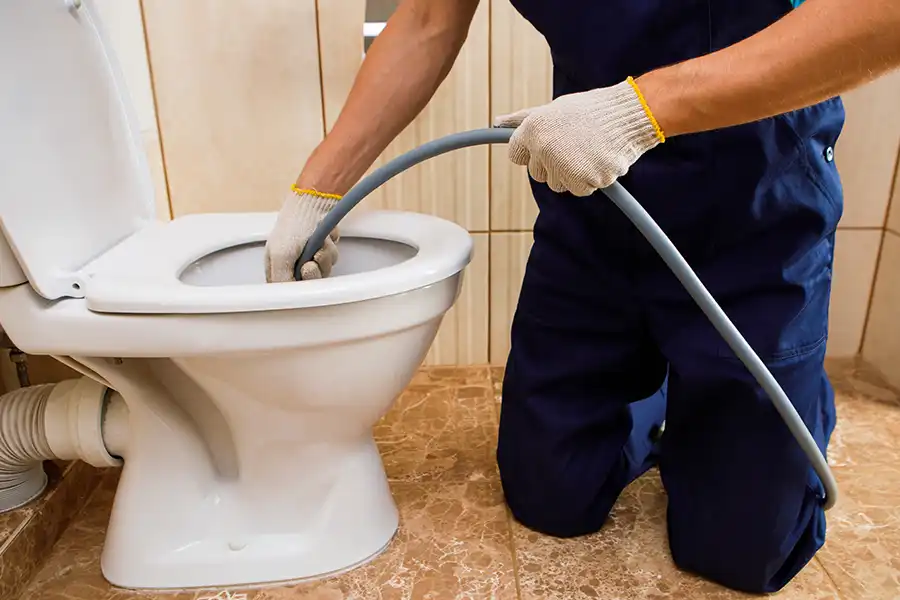 Sewer & Septic Specialist—A professional plumber unclogging a blocked toilet with hydrojetting in a home bathroom in Decatur, IL.